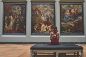 A woman sitting in an art gallery looking at paintings